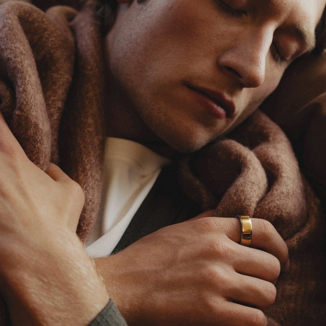 Man sleeping with a blanket while wearing a gold Oura Ring 4