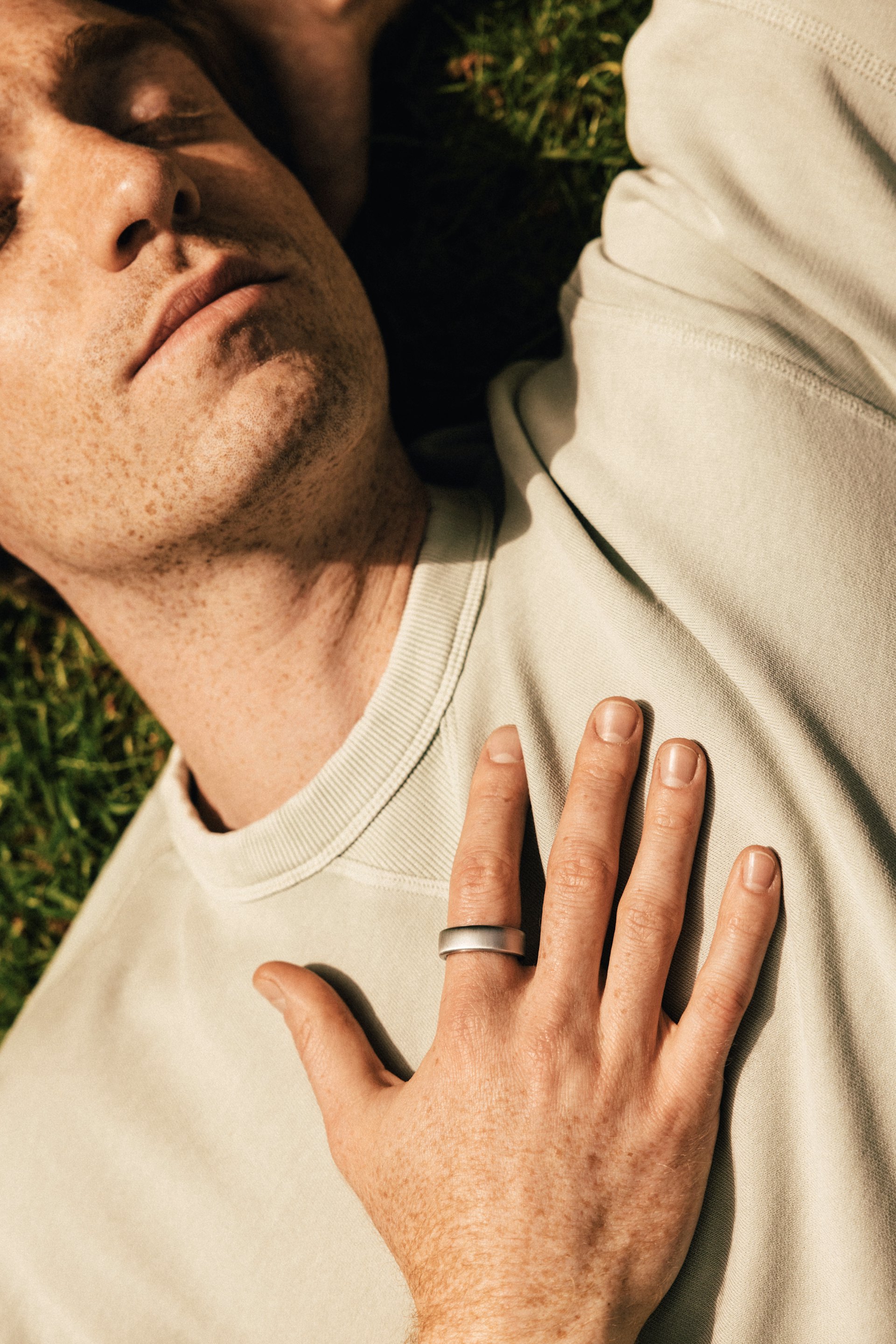 A man laying on grass with his right hand on his chest and an Oura Ring on his index finger.