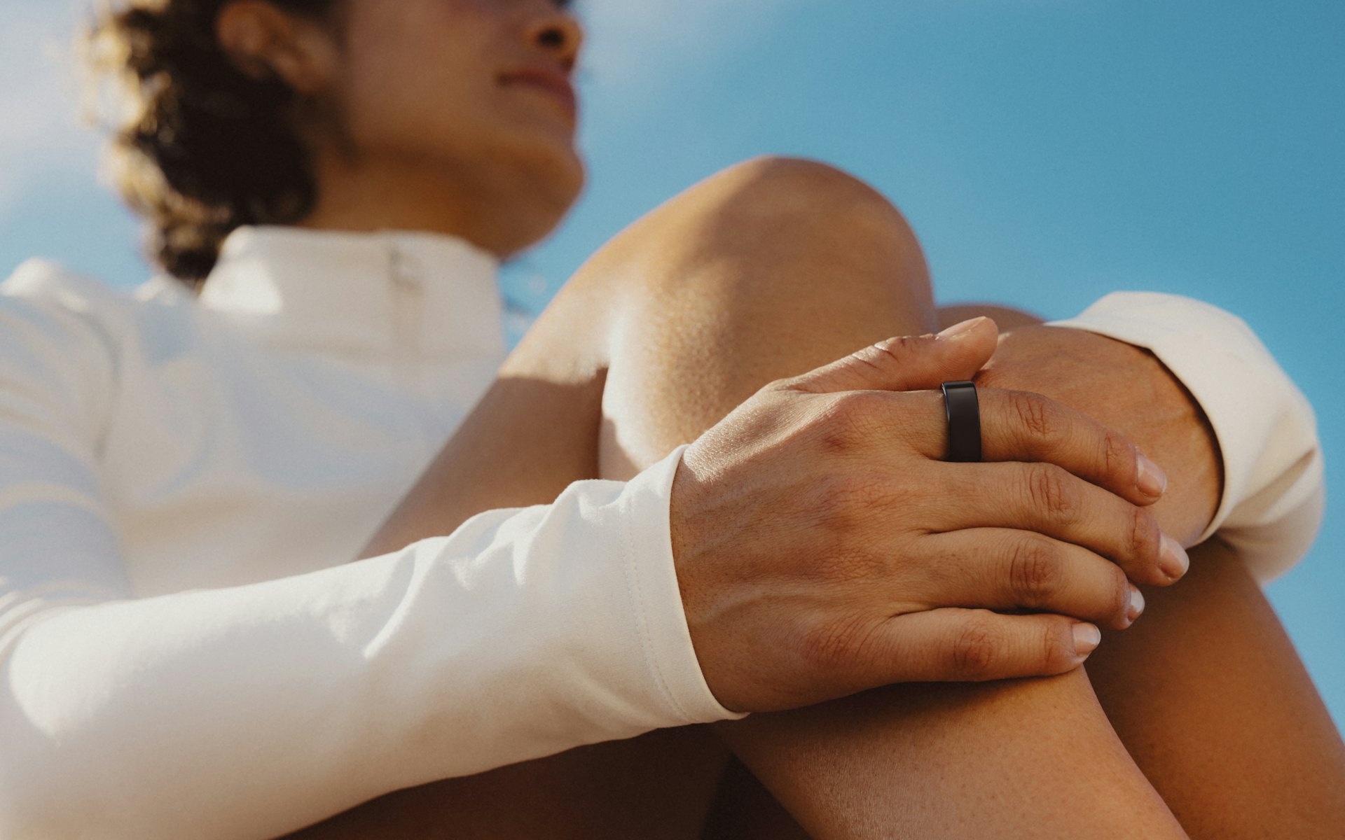 Women sitting resting her hand on knee wearing an Oura Ring with an app overlay